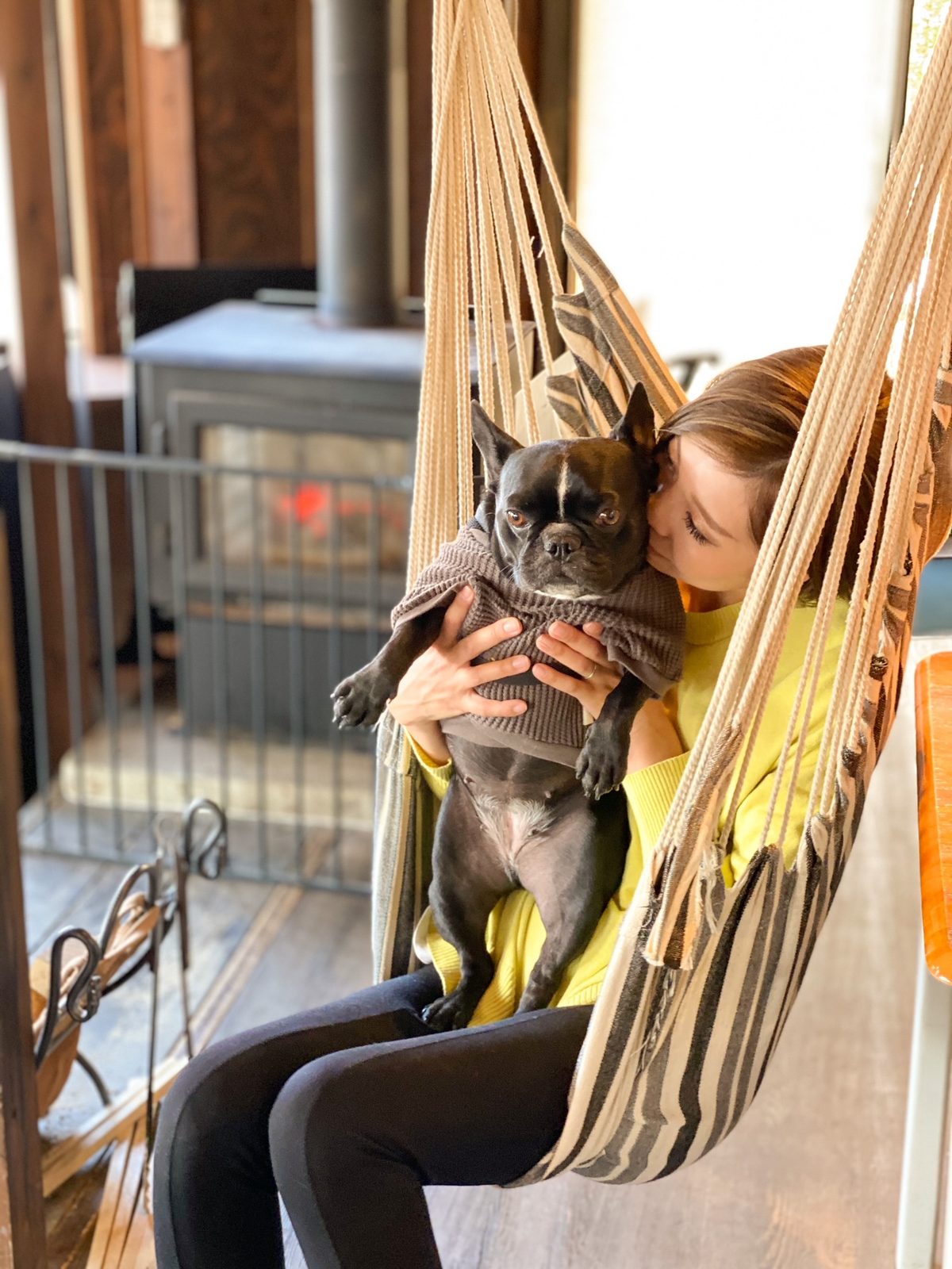 ハンモックに揺られながら愛犬を抱く女性。奥には薪ストーブ