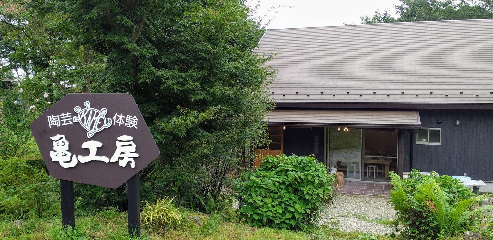 「陶芸体験 亀工房」の看板と、緑に囲まれた工房の外観