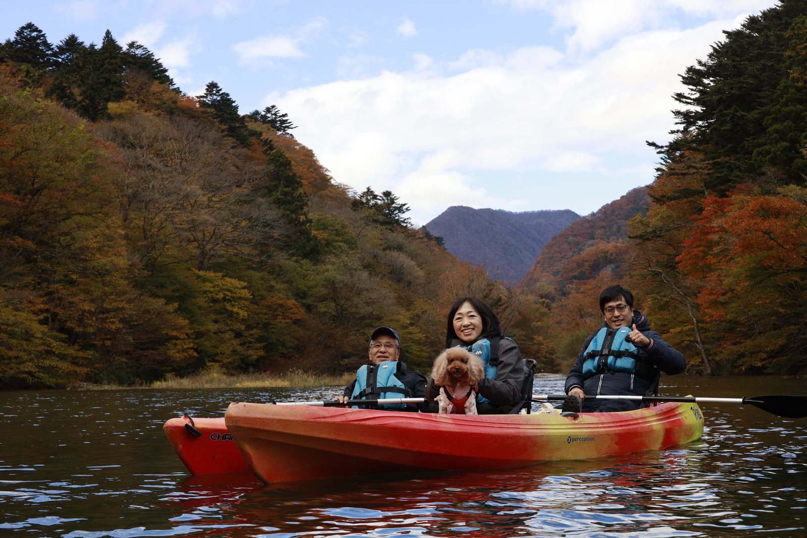 紅葉の山に囲まれた湖を、愛犬を乗せてカヌーで進む人たち